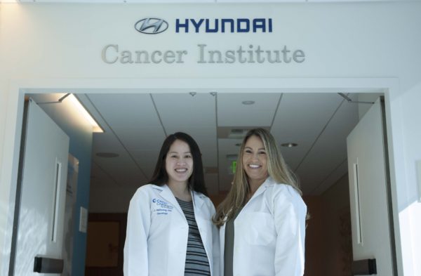Two female doctors smile in lab coats in front on Hyundai Cancer Institute's sign 